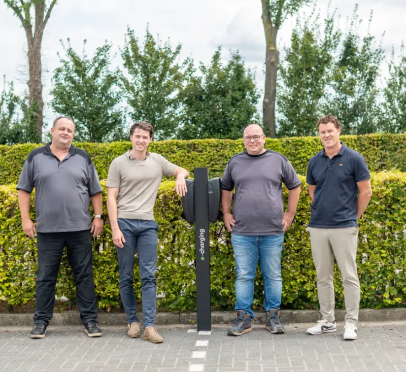Het team van E-Charging bij een laadpaal met eigen branding op de parkeerplaats bij het kantoor