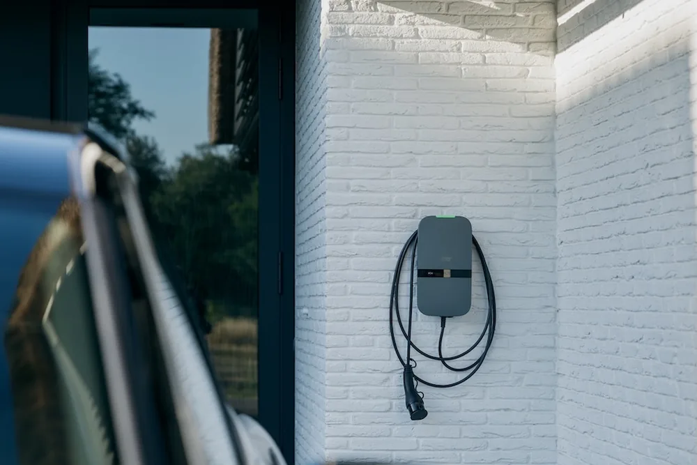 Peblar Home laadpaal aan een witte gevel, met de laadkabel opgehangen