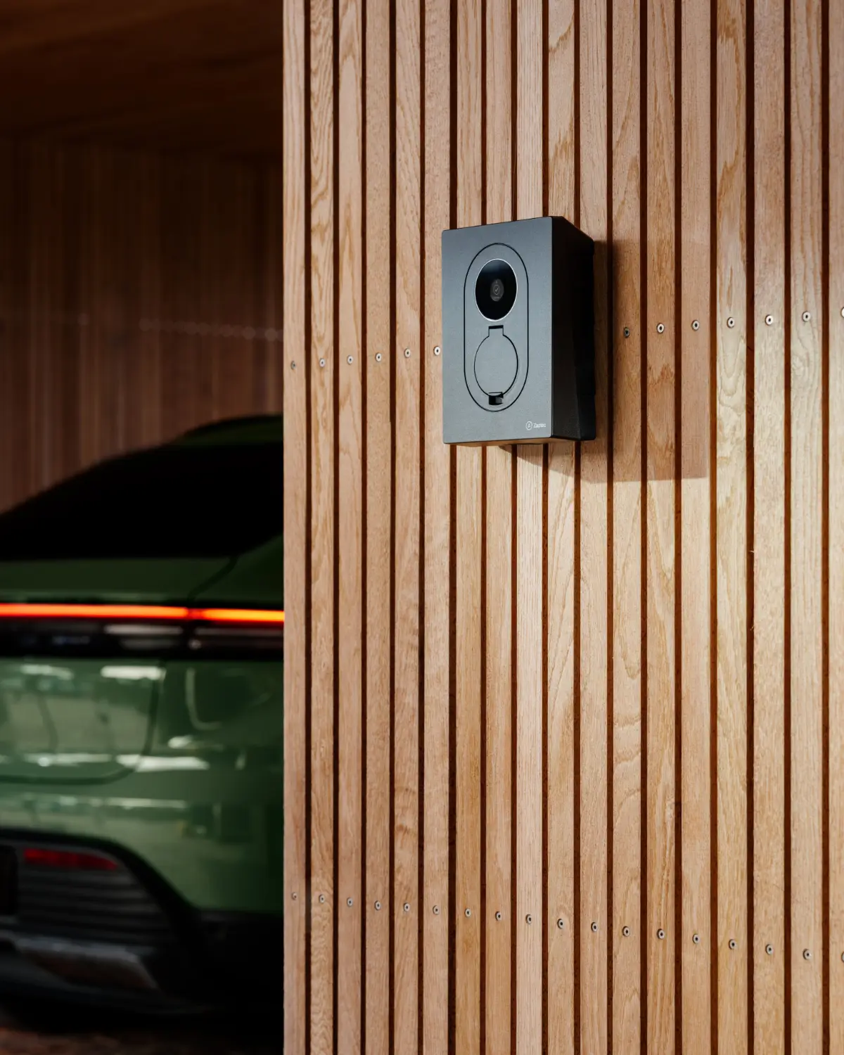 Witte Zaptec Go aan een houten gevel, met een elektrische auto ervoor
